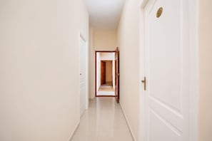 A hallway with white walls and doors, leading to a room with a wooden door. - Fabhotel Nimalan Residency Sholinganallur (Chennai)