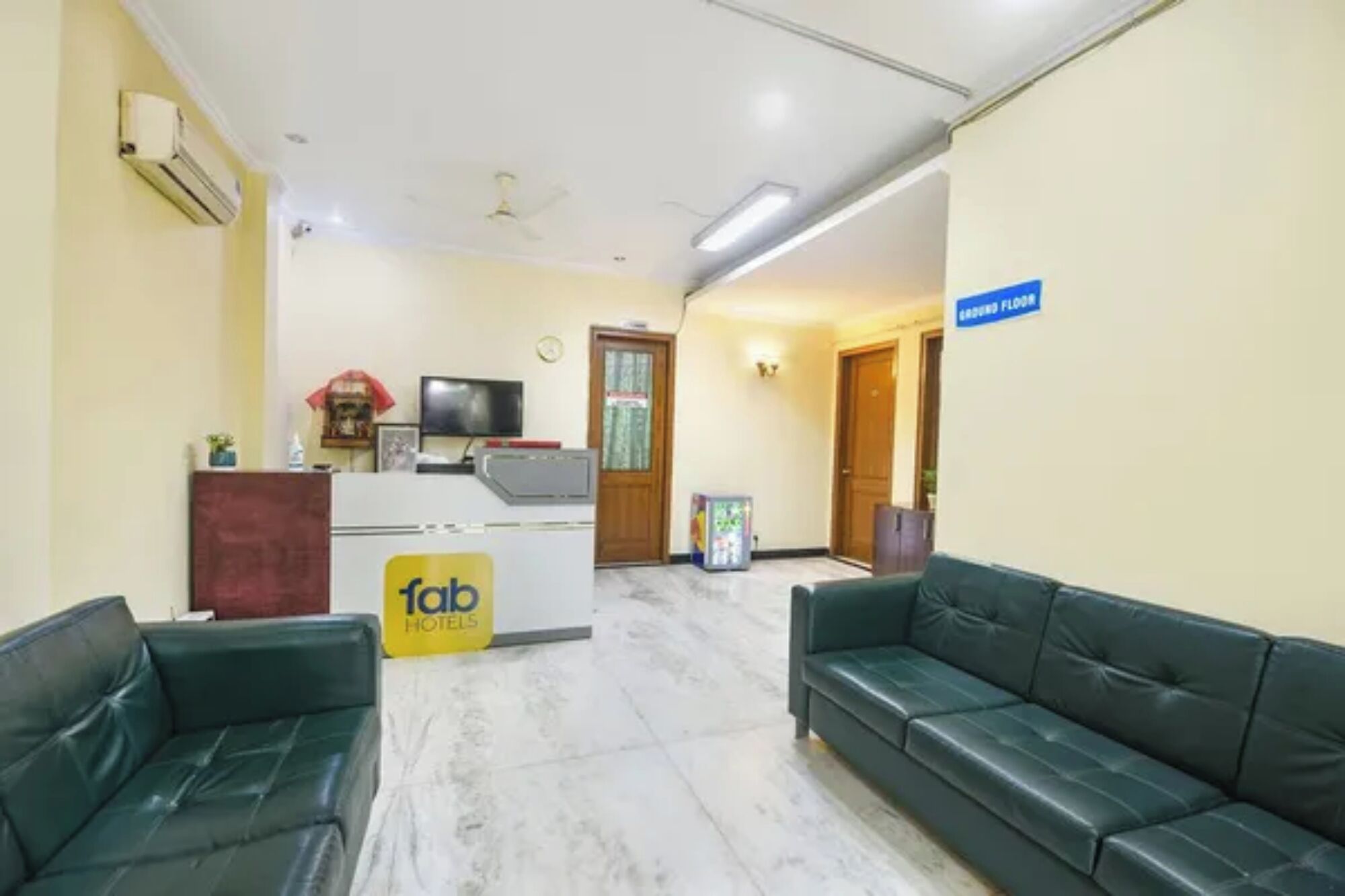 A hotel lobby with a reception desk, two green leather sofas, a TV, and a sign indicating the ground floor.