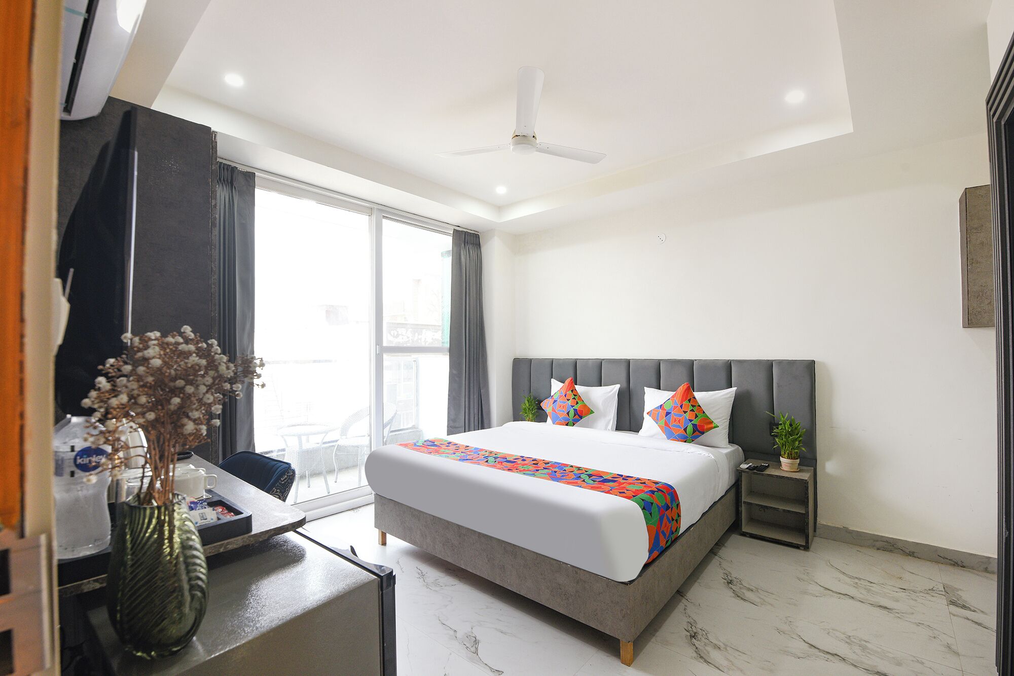 A hotel room with a bed, bedside table, nightstand, and a large window.