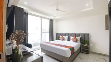 A hotel room with a bed, bedside table, nightstand, and a large window.