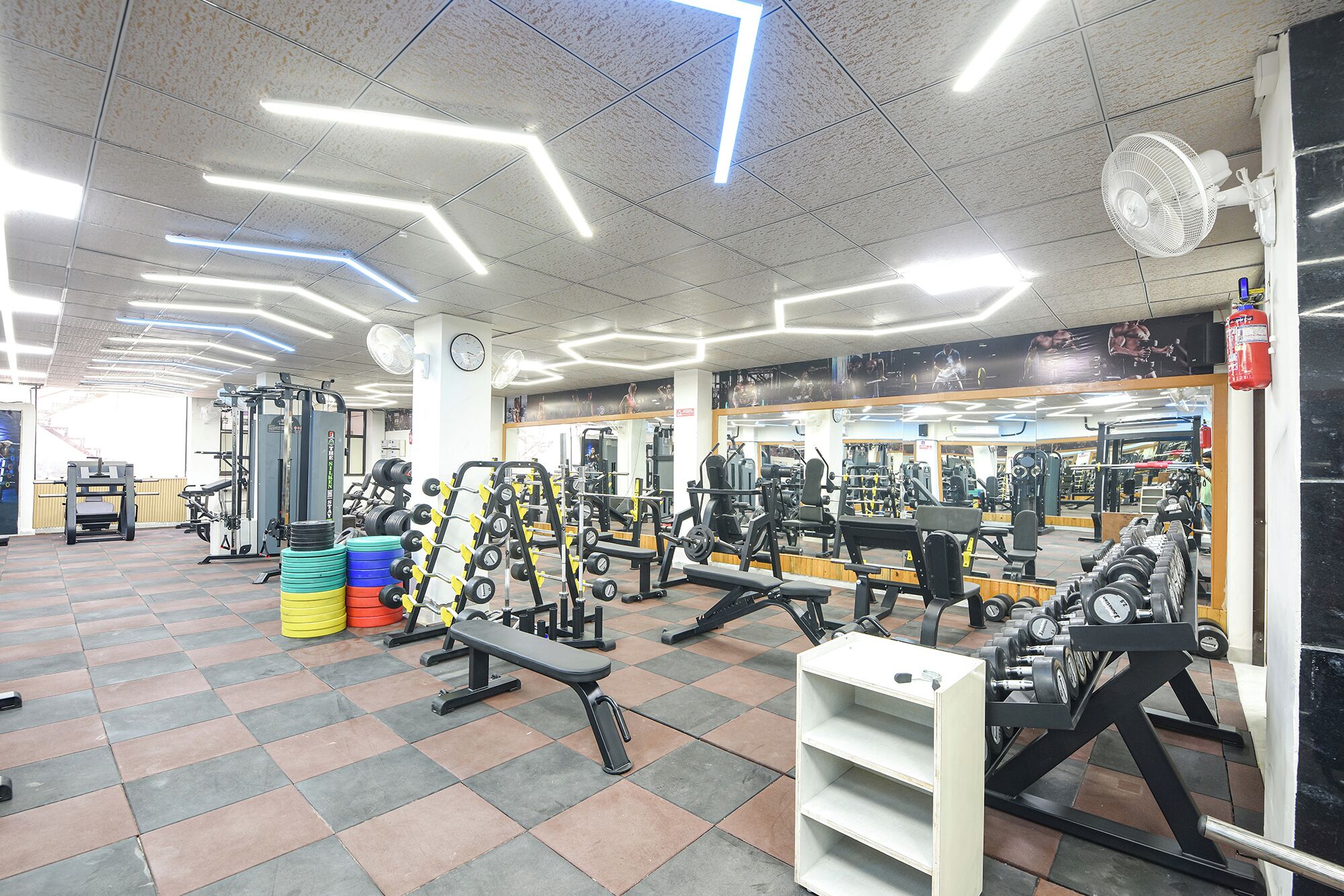 A gym with various exercise equipment, a clock, and a fire extinguisher.