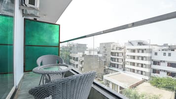 A balcony with wicker furniture and a glass partition, overlooking a cityscape with multiple buildings.