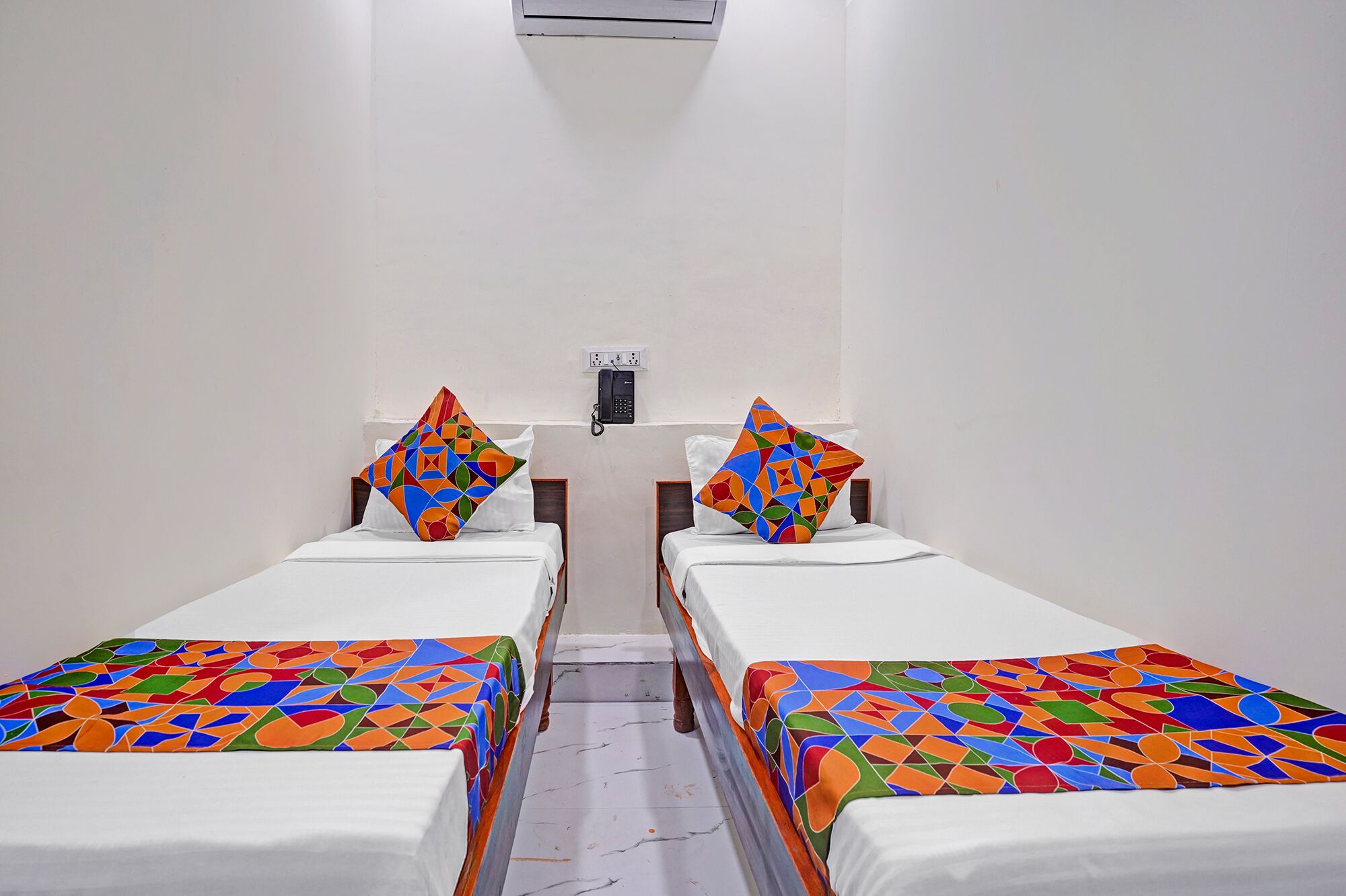 A room with two beds, each with a colorful geometric-patterned bedspread and pillows.