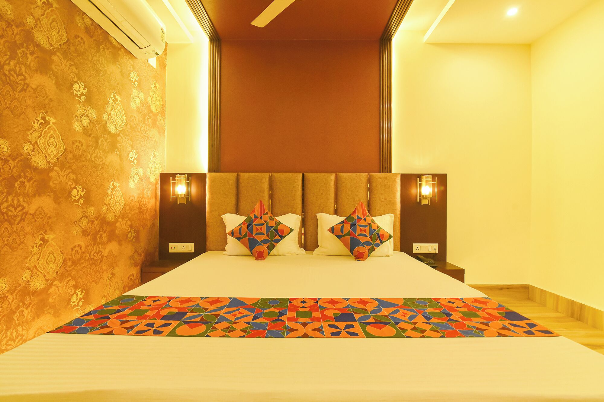 A hotel room with a bed, patterned wallpaper, and wall-mounted light fixtures.