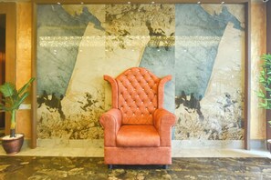 Un fauteuil moelleux dans un hall d’entrée, avec un mur de marbre et des plantes en pot.