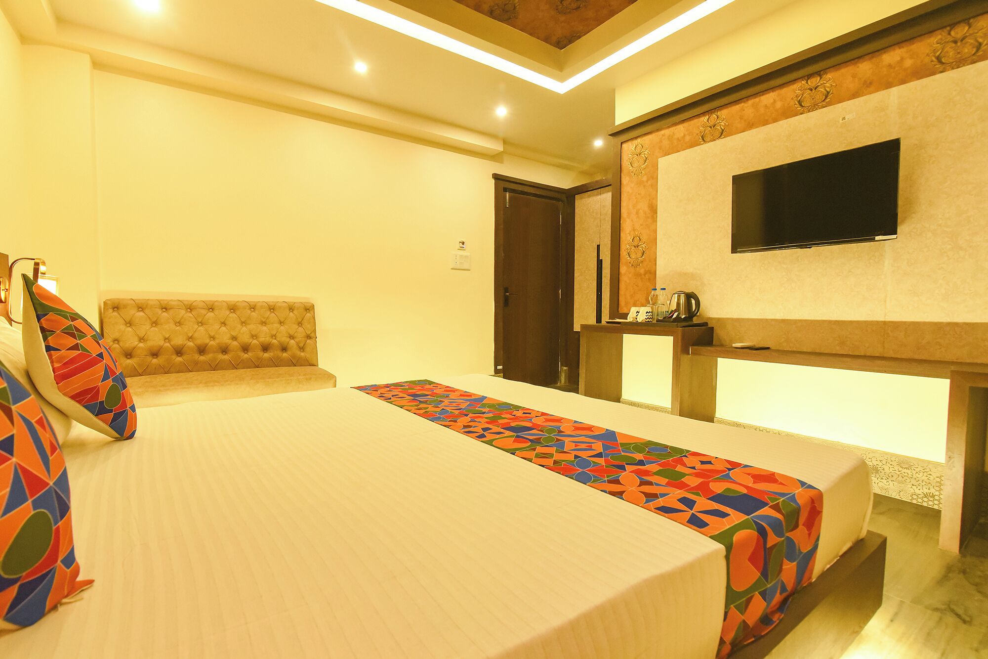 A hotel room with a bed, a television mounted on the wall, and a desk with a mirror.