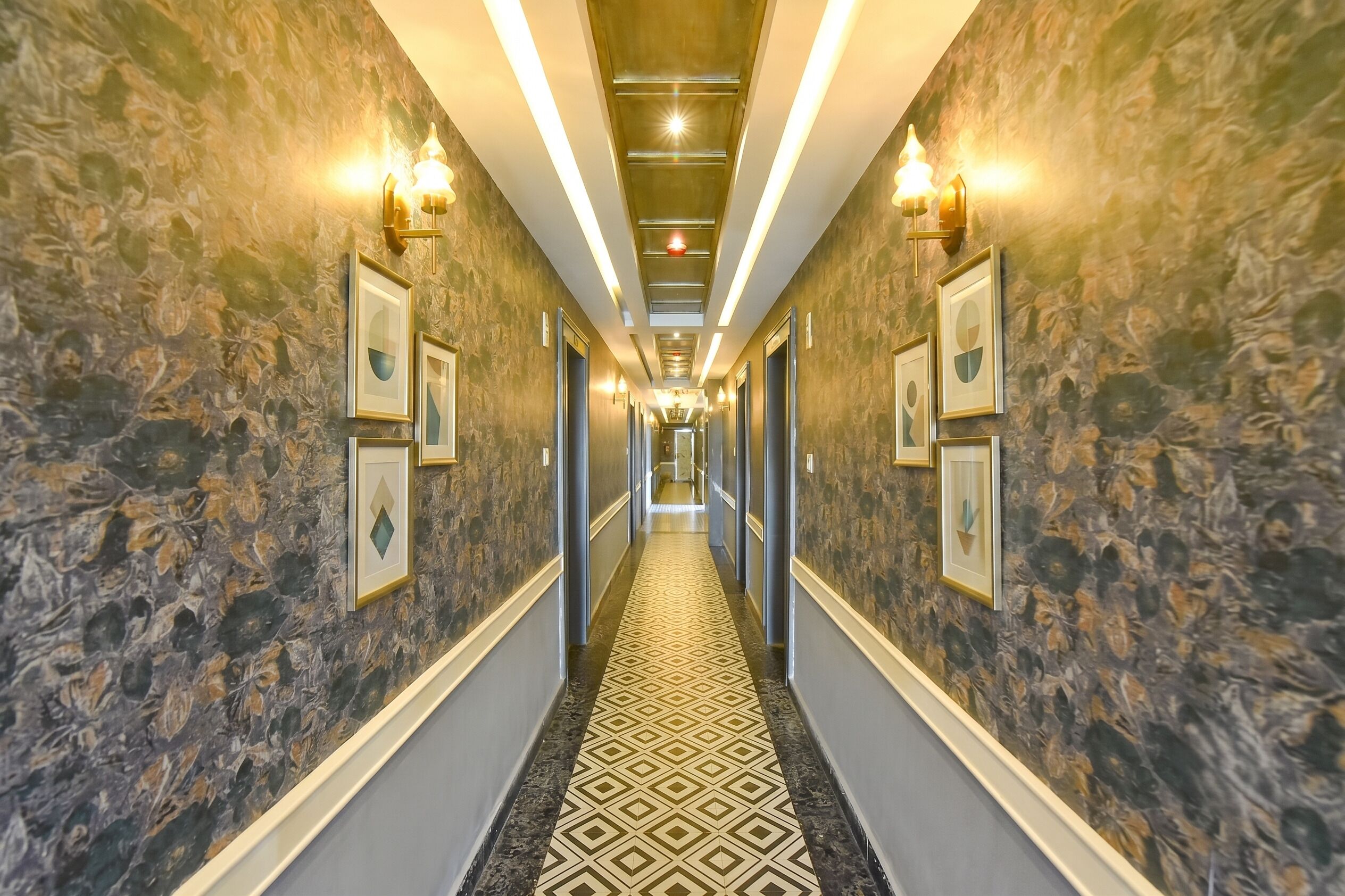 A hallway with patterned walls, framed artwork, and recessed lighting.