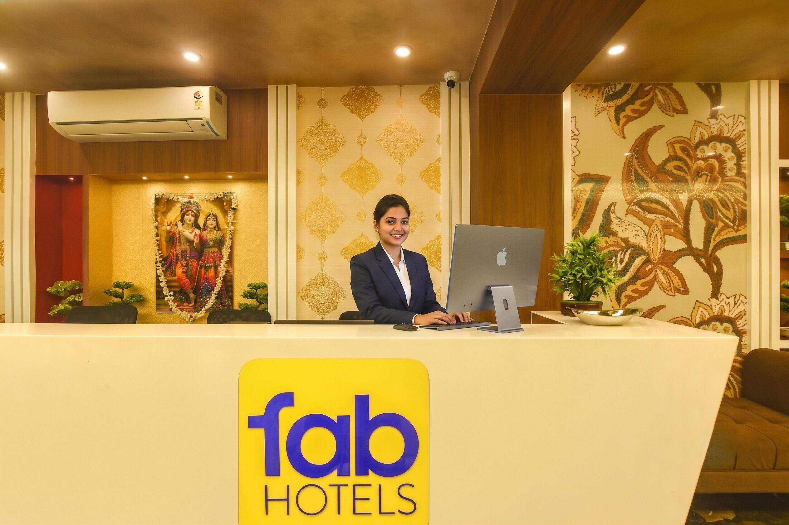 Ein Hotelrezeptionstresen mit einem Computer, eine Wand mit floralen Mustern und ein Schild mit der Aufschrift 'fab hotels'.