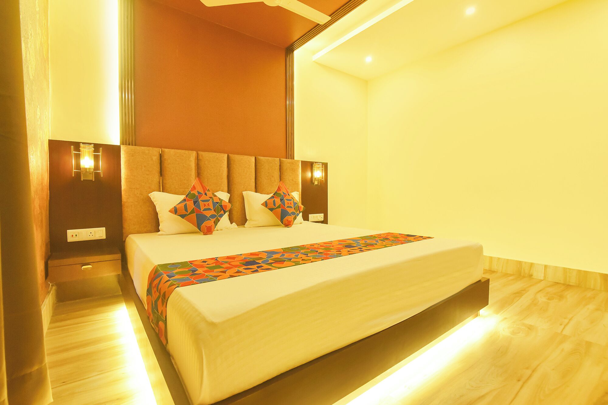 Una habitación de hotel con cama, cabecera, lámparas de noche y mesita de noche.
