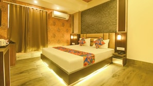 A hotel room with a large bed, an air conditioning unit, a bedside table, and a nightstand with a phone. - Fabhotel Prime Grand Plaza (Barakpur)