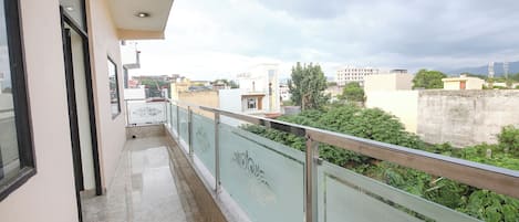 Un balcón con barandilla de vidrio, ventilador de techo y vistas de edificios circundantes.