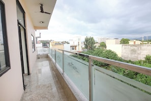 Un balcón con barandilla de vidrio, ventilador de techo y vistas de edificios circundantes.