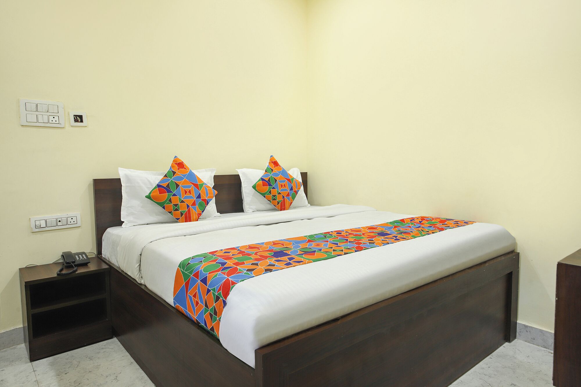 A hotel room with a bed, a nightstand, and a bedside table.