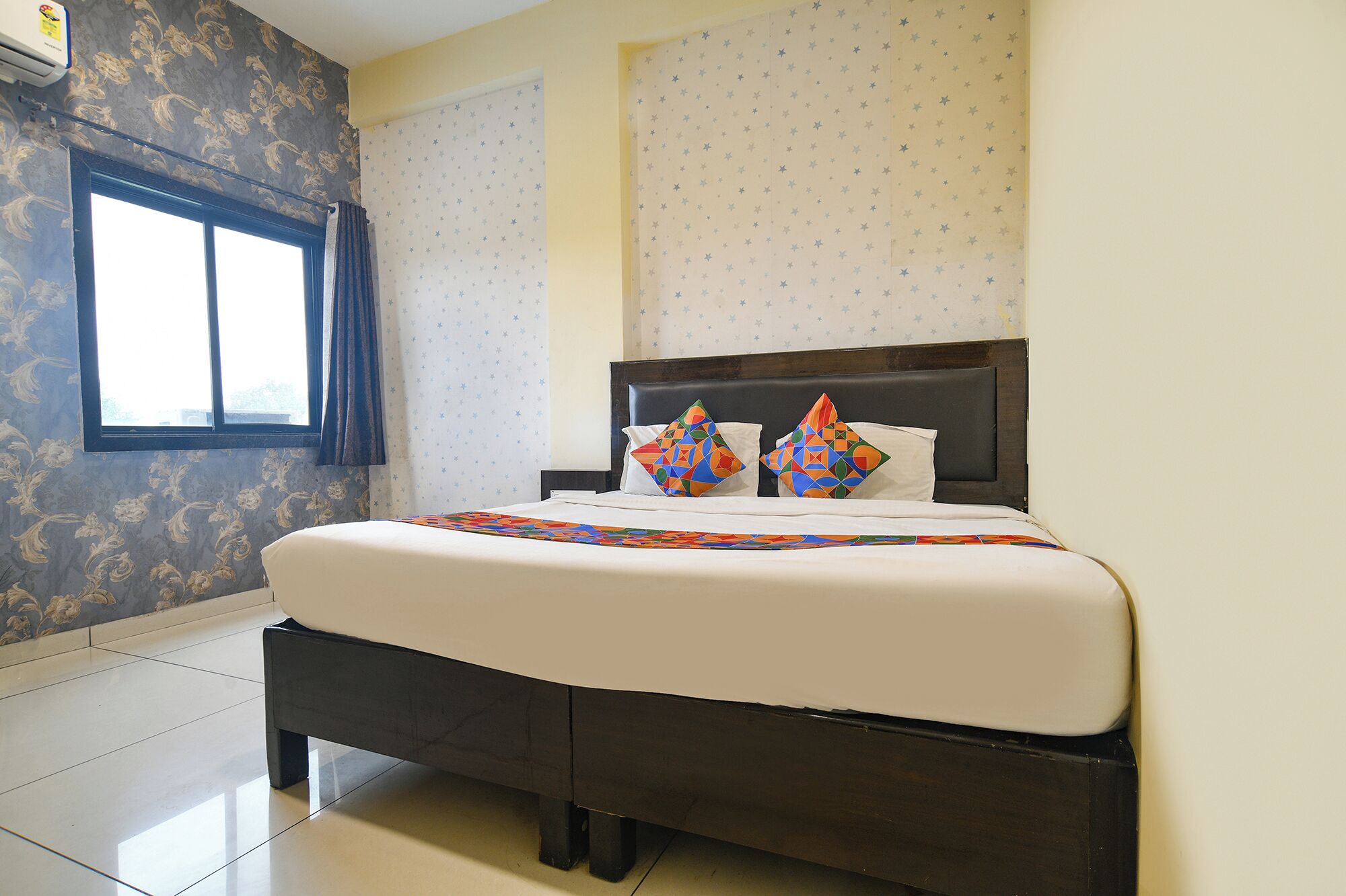 A hotel room with a large bed, a window, and patterned wallpaper.