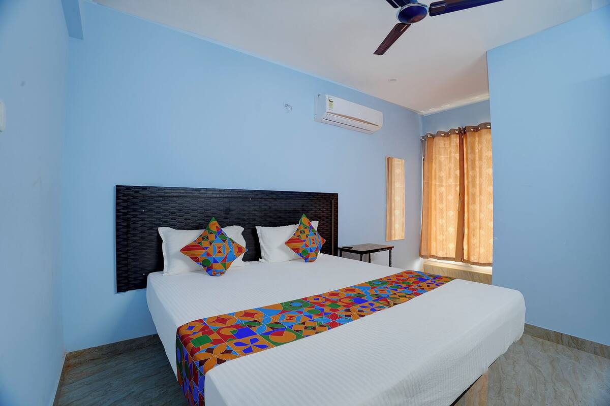 A hotel room with a bed, a ceiling fan, an air conditioning unit, and a window with curtains.