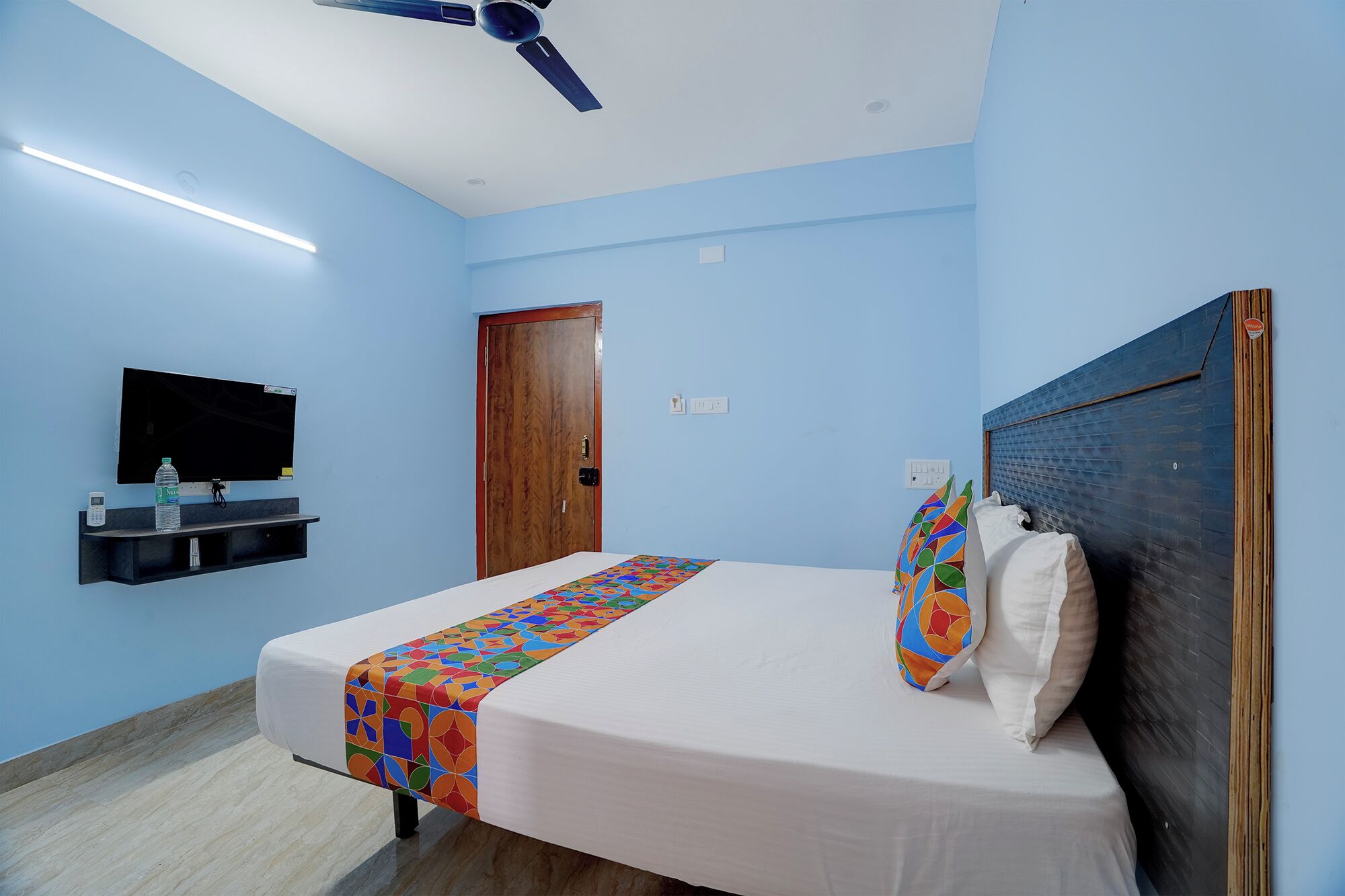 A bedroom with a bed, a television on the wall, a ceiling fan, and a wooden door.