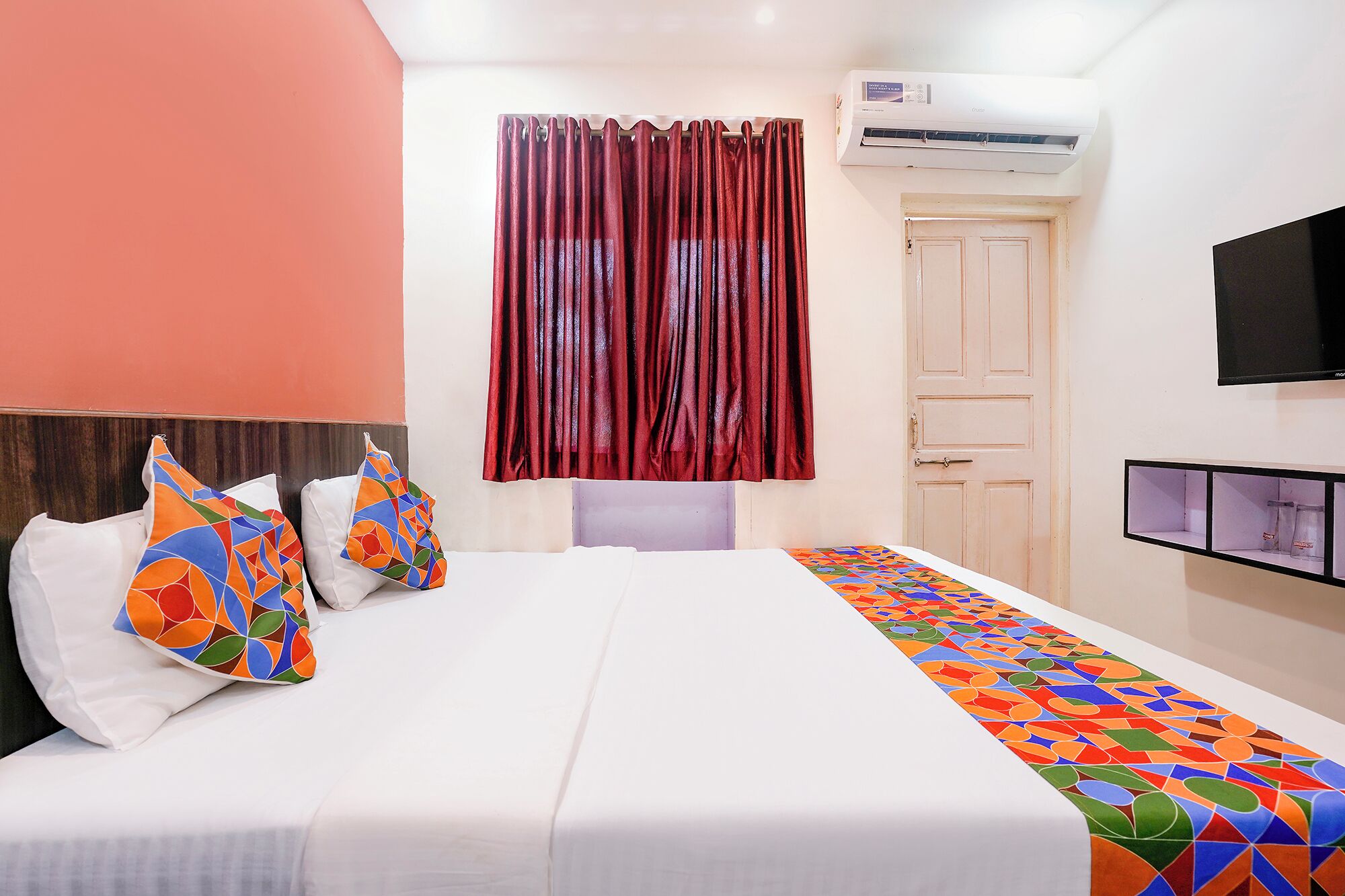 Een hotelkamer met een bed, een televisie, een airconditioner en een deur.