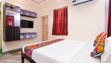 A hotel room with a bed, a TV mounted on the wall, a wardrobe, and an air conditioning unit.