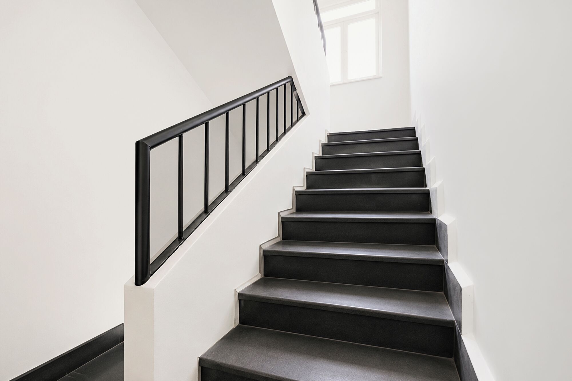 Una escalera con barandilla negra y paredes blancas.