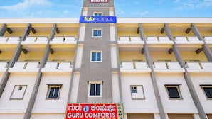 Un immeuble à plusieurs étages, avec des enseignes indiquant « Rooms » et « fabHOTELS », arborant la marque « GURU COMFORTS », et doté d’une série de fenêtres et de balcons.