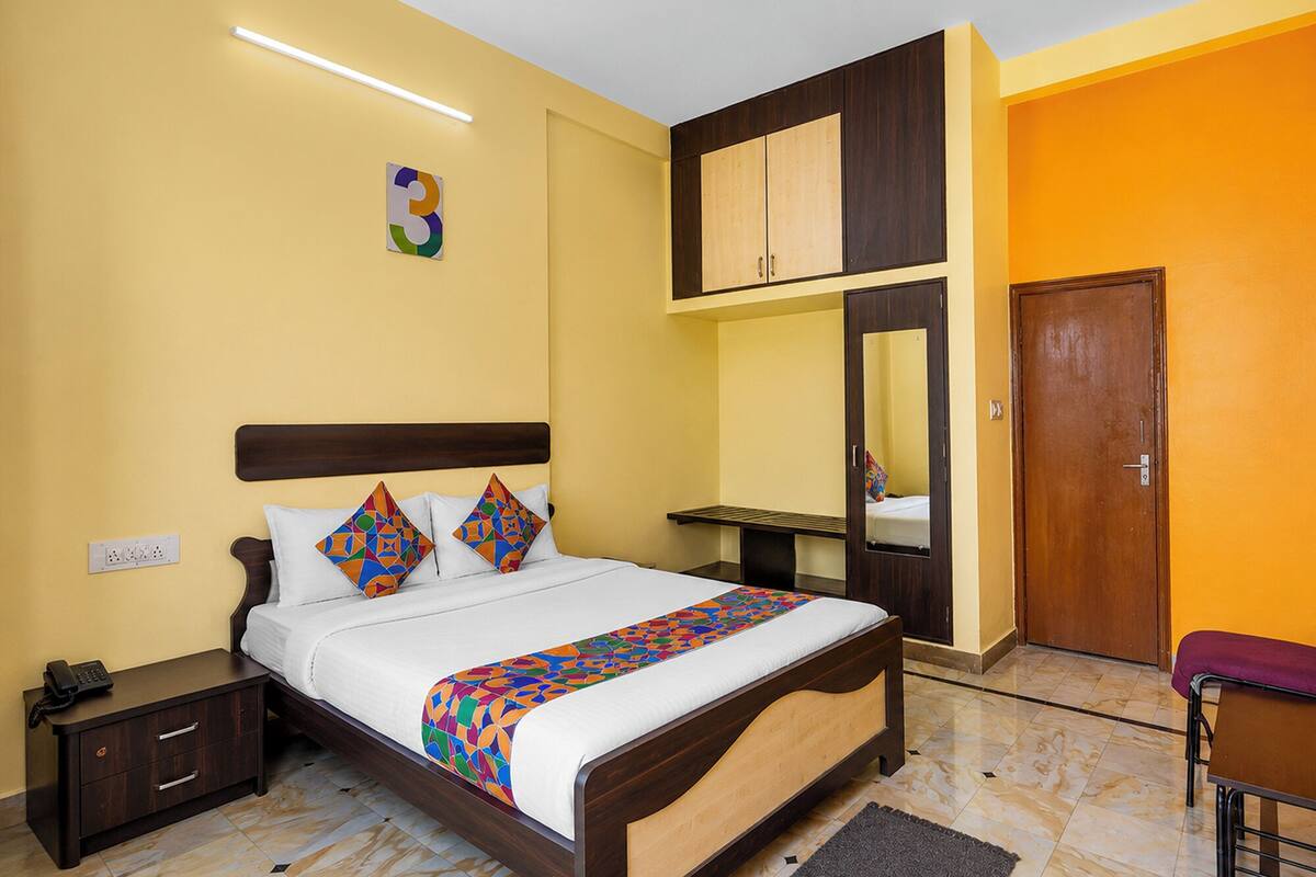 Een hotelkamer met een bed, nachtkastje, kapstok, spiegel en een deur.
