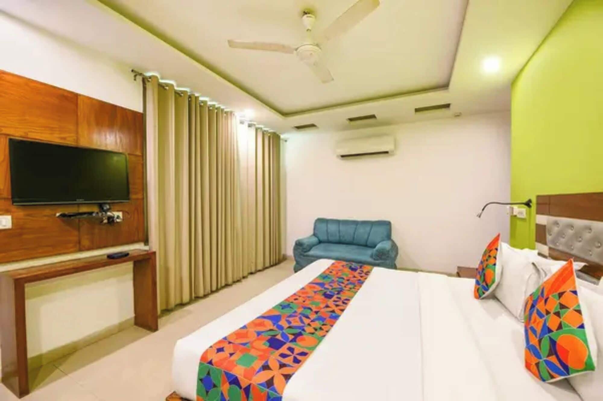 A hotel room with a bed, a television, a ceiling fan, and a window with curtains.