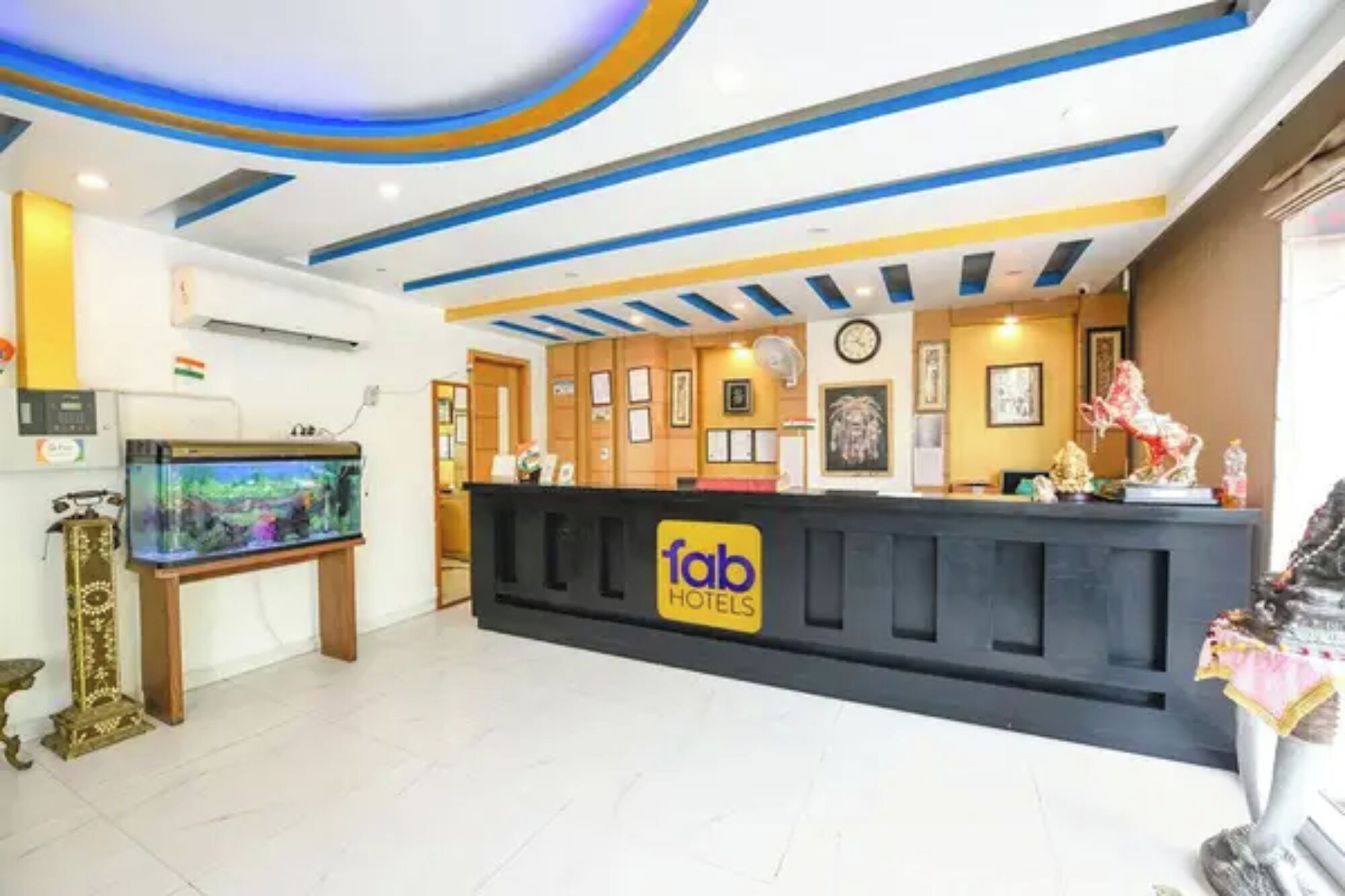 A hotel reception area with a reception desk, a clock, framed pictures on the wall, and a decorative statue.