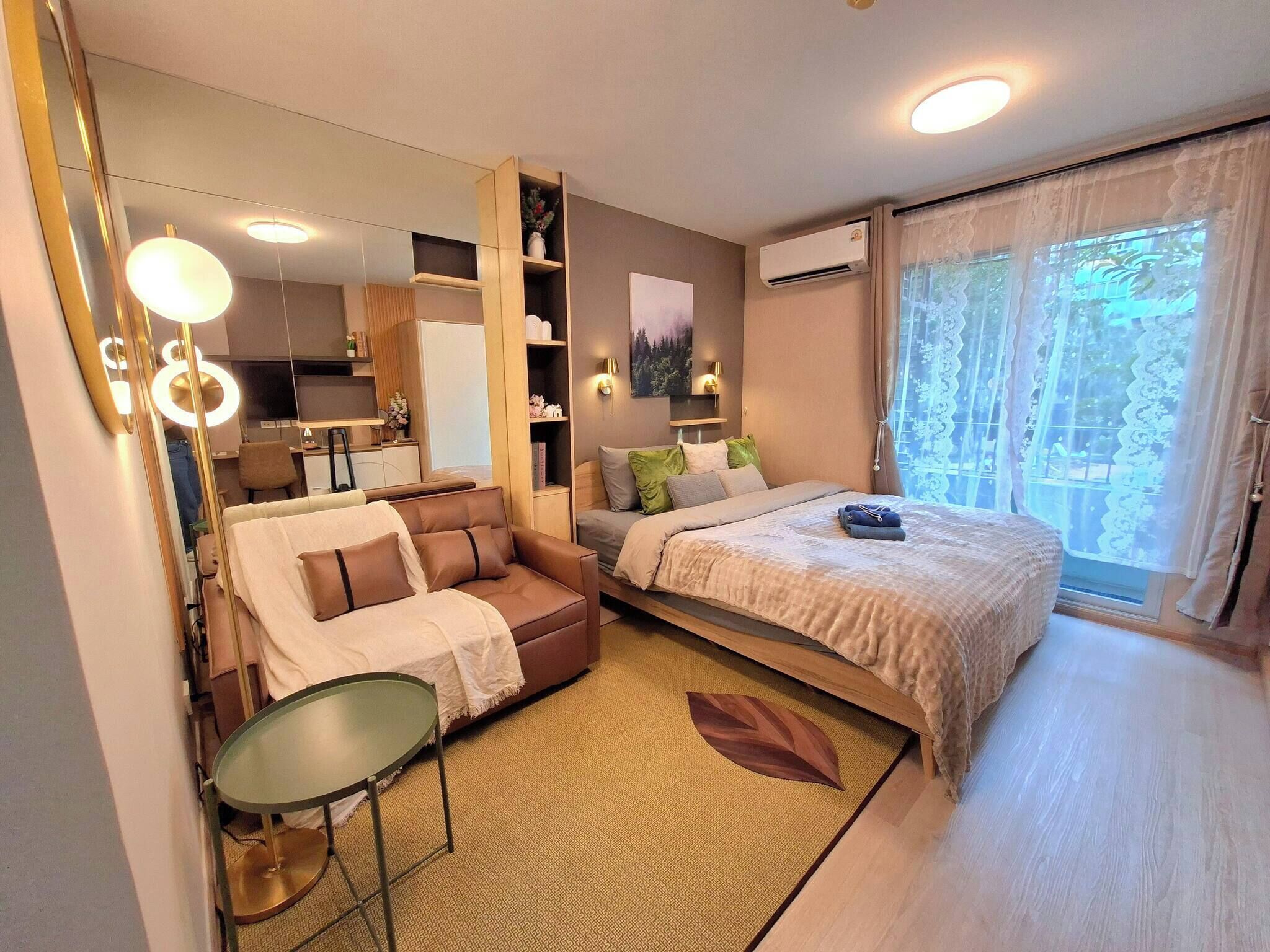 Moderni hotellihuone, jossa on sänky, sohva, pieni pöytä, peili ja ikkuna, jossa on verhot.