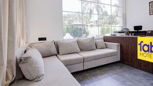 A modern hotel room with a large window, a sofa, a reception desk, and a view of palm trees.
