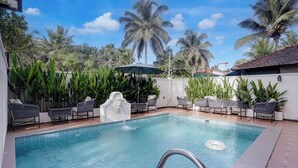 A swimming pool with lounge chairs and a decorative fountain, surrounded by palm trees and greenery.