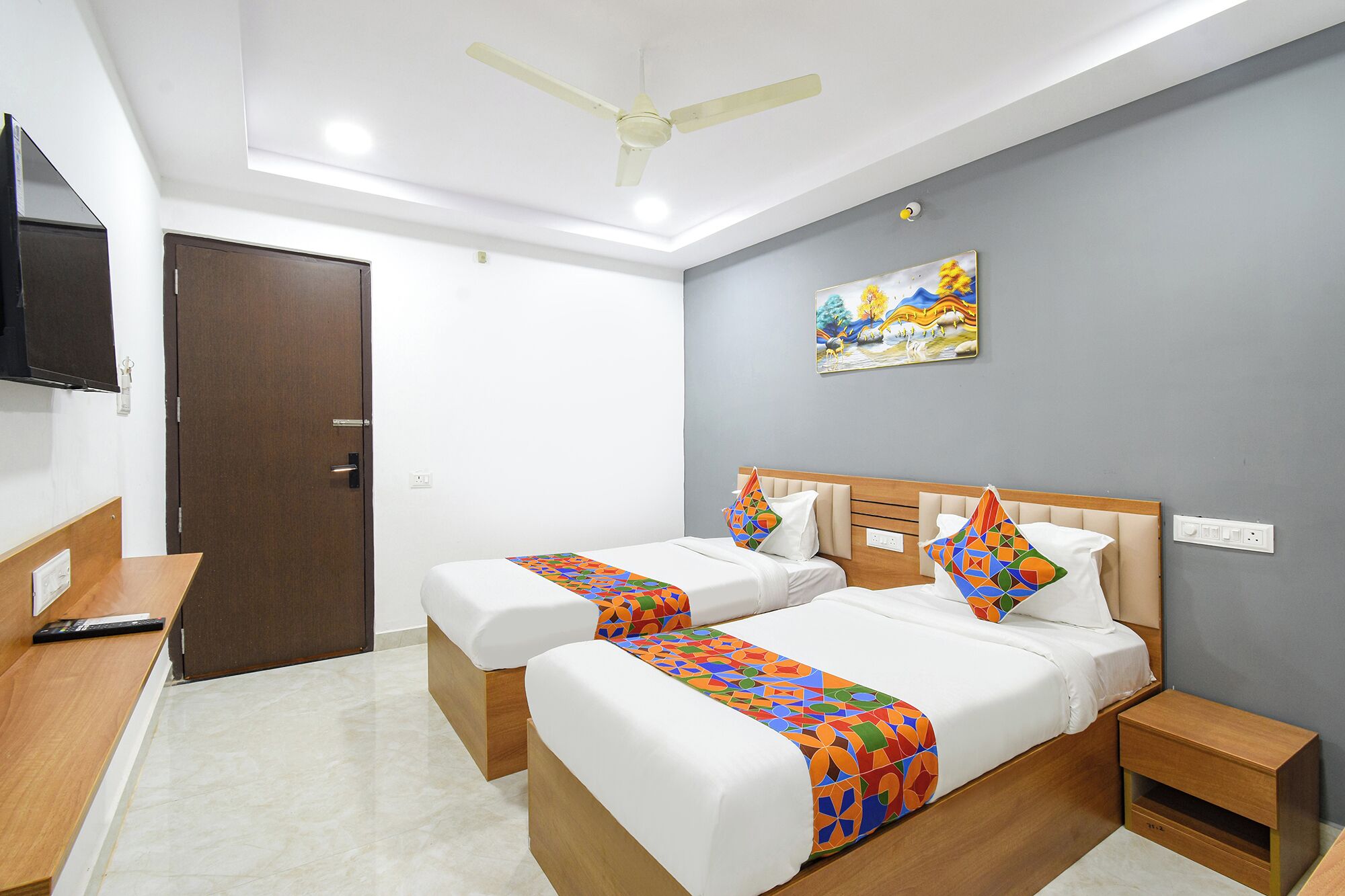 A hotel room with two beds, a desk, a TV, and a ceiling fan.