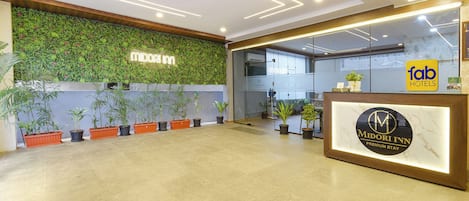 Zona de recepción con pared verde, plantas en macetas y mostrador de recepción con un logotipo.