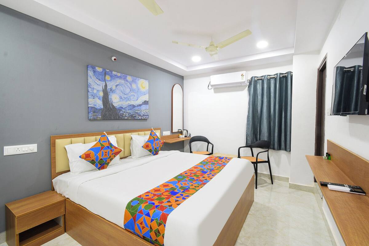 Habitación de hotel con cama, escritorio, silla, televisor y un cuadro en la pared.