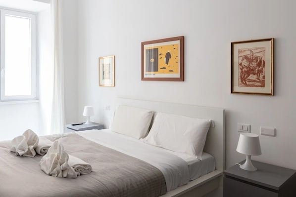 Une chambre d’hôtel avec un lit, une table de chevet, une lampe et trois œuvres d’art encadrées accrochées au mur.
