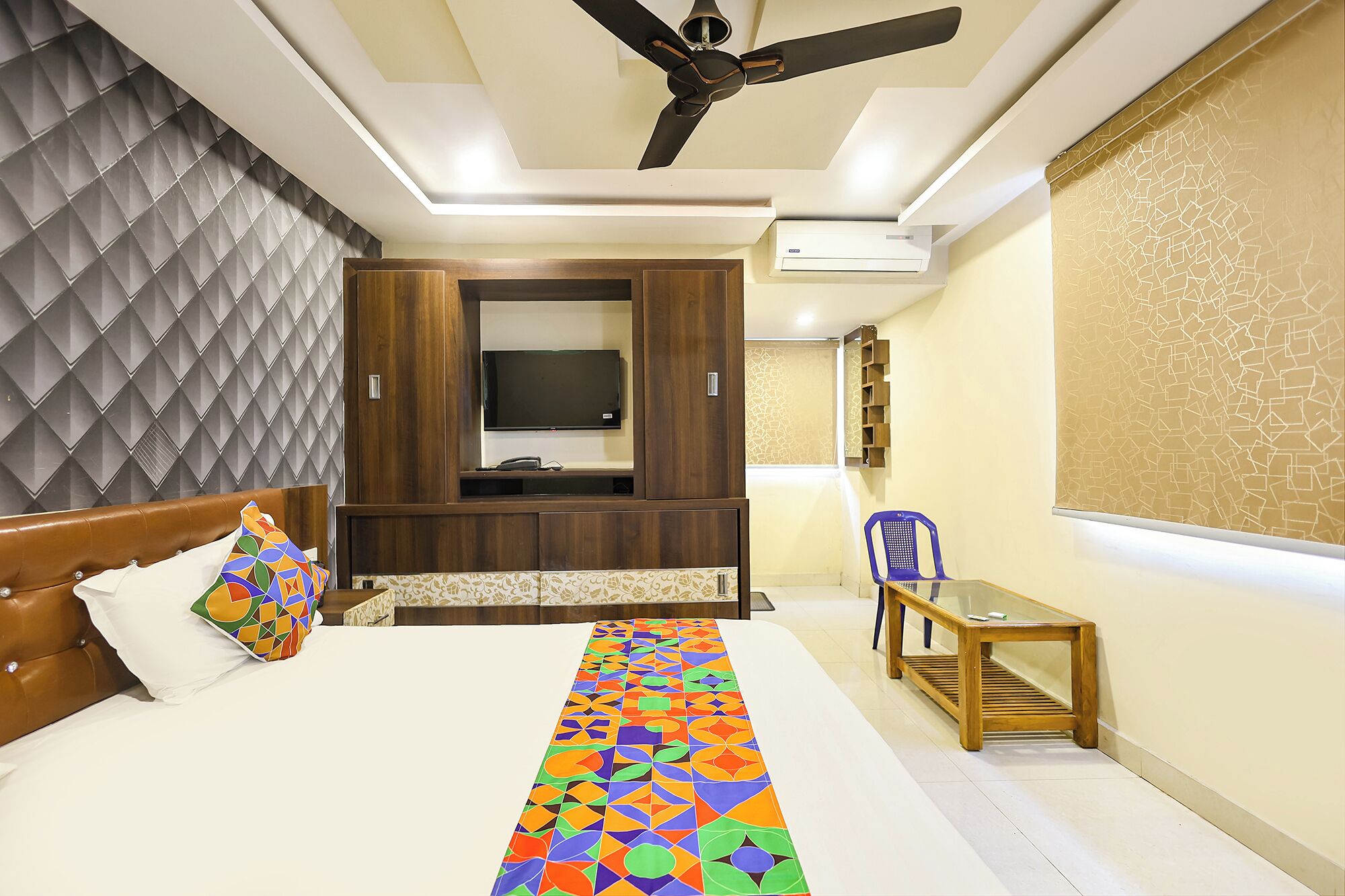 A bedroom with a bed, a TV, a ceiling fan, a desk, and a chair.