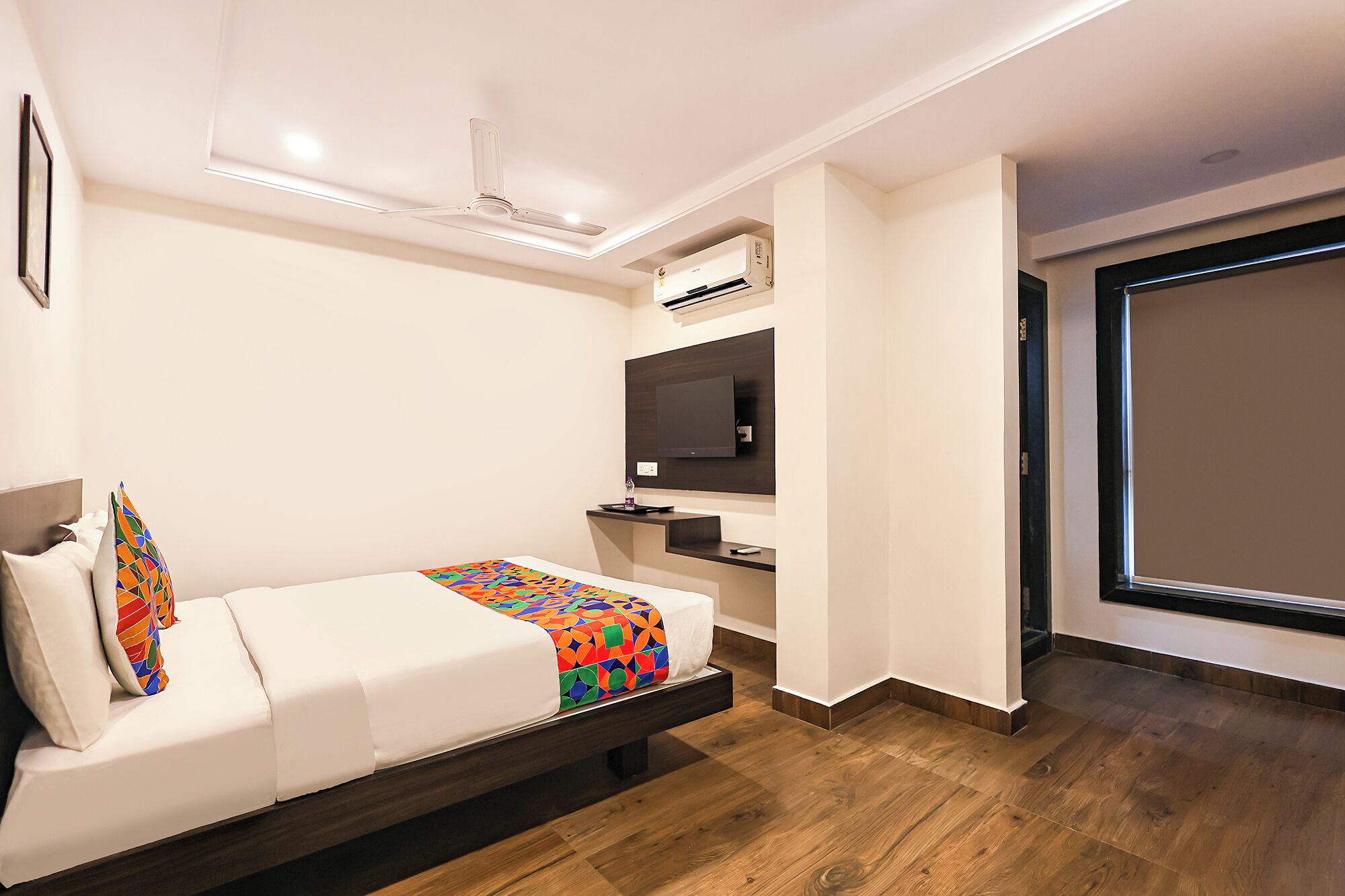 Una habitación de hotel moderna con una cama, un televisor, un equipo de aire acondicionado y una puerta corrediza al exterior.