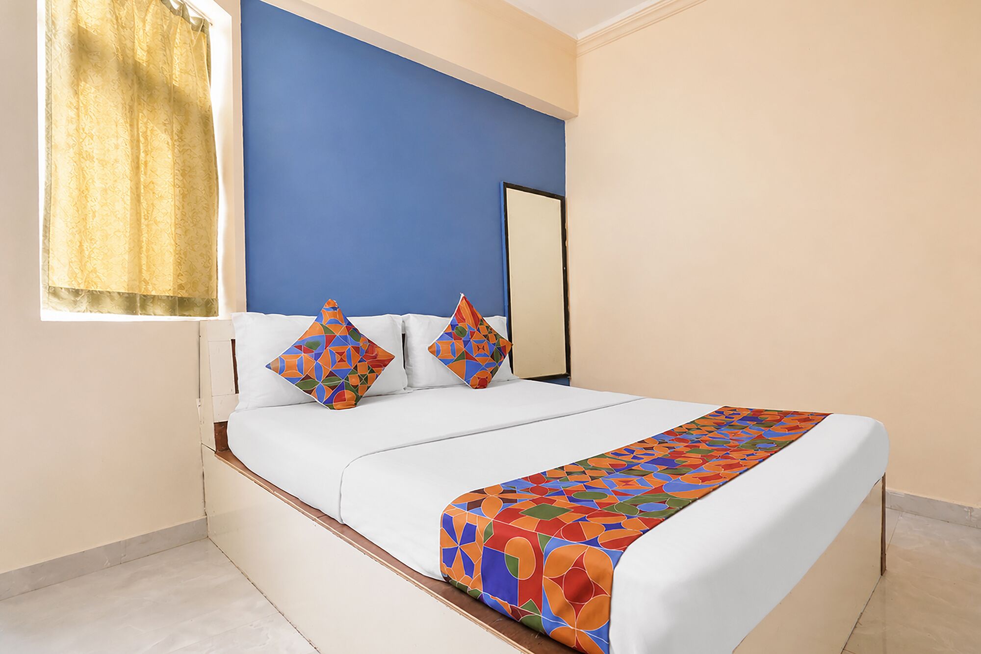 Una cama con una colcha de diseño geométrico y colores vivos, un cabecero blanco y dos almohadas decorativas.