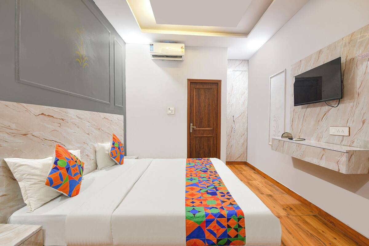 Una camera da letto con un letto, cuscini, una TV a muro e un condizionatore.