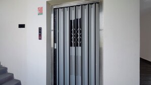 Una puerta de seguridad metálica con diseño de barras verticales, una escalera a la izquierda y un letrero que dice 'LIFT' encima.
