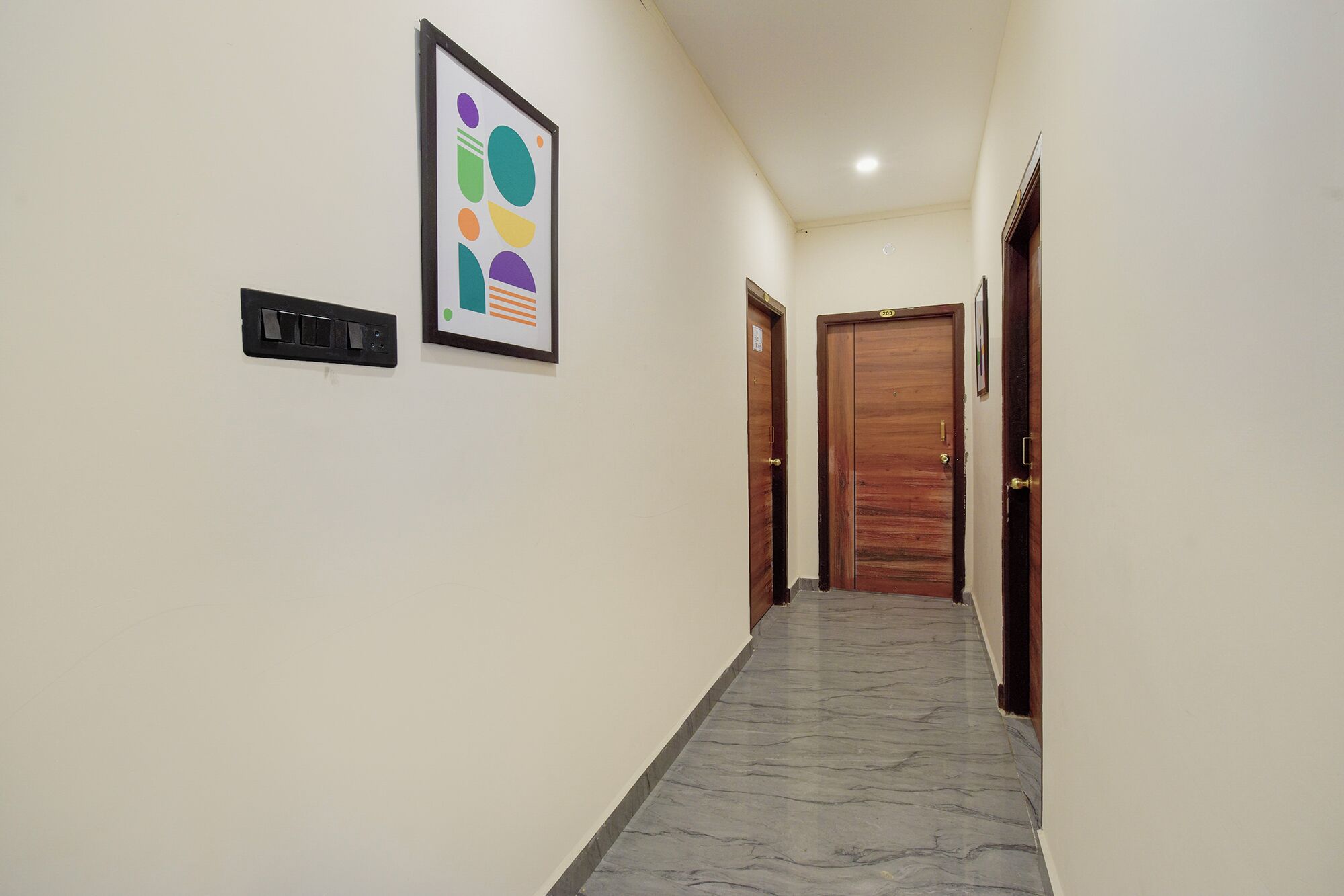 A hallway with a marble floor, a framed abstract artwork, a black intercom, and two wooden doors.