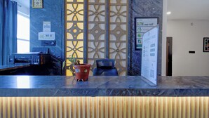 Un mostrador de recepción de hotel con una impresora Canon, una planta en maceta y un panel decorativo en la pared.