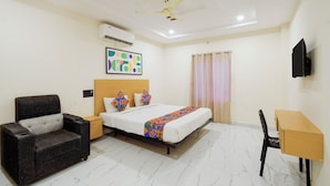 Habitación de hotel con cama, escritorio, silla, sofá, aire acondicionado, ventilador de techo, un cuadro y ventana con cortinas.