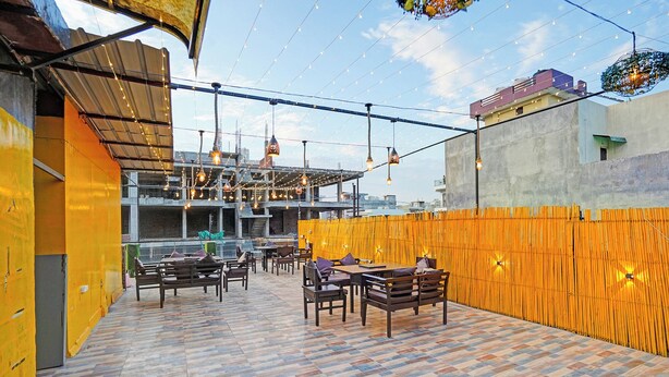 An outdoor dining area with tables and chairs, string lights, and a bamboo fence. - Fabhotel Pillow & Pesto (Noida)