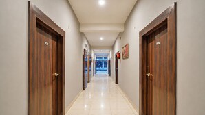 A hotel hallway with wooden doors, numbered room signs, and framed artwork on the walls. - Fabhotel Pillow & Pesto (Noida)