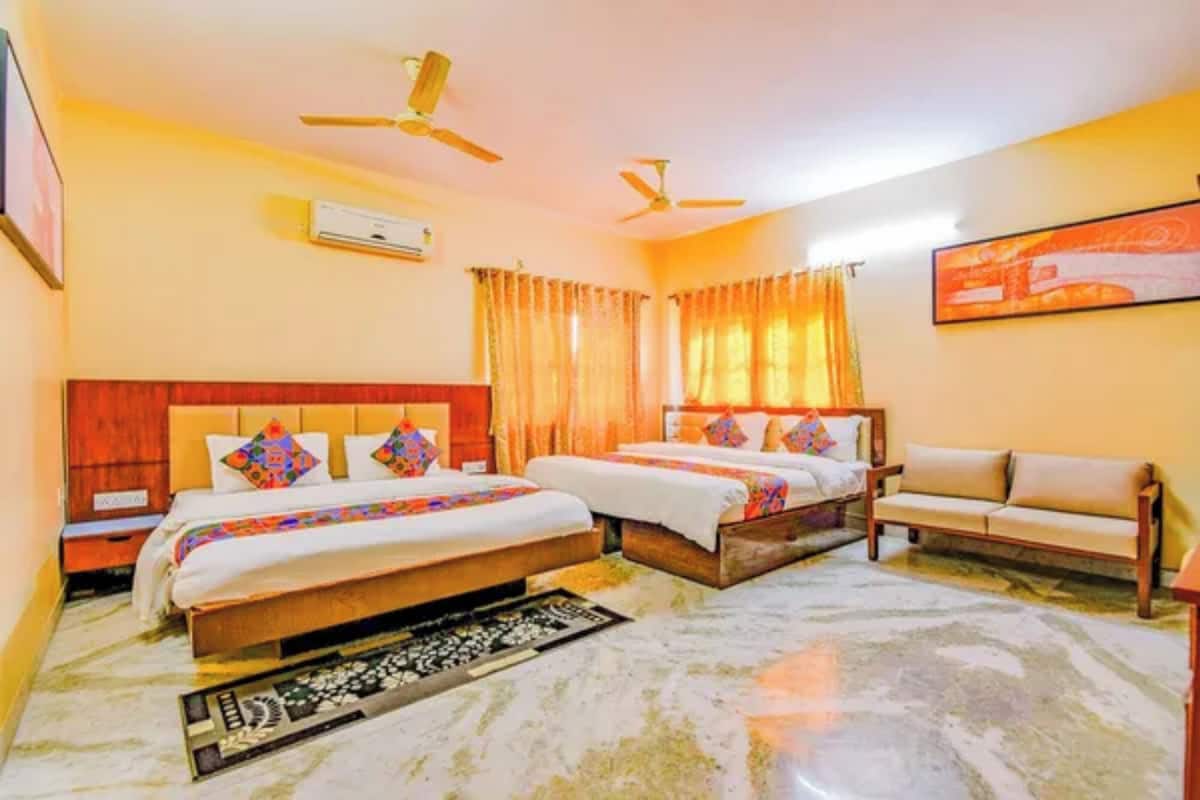 A hotel room with two beds, a sofa, a ceiling fan, and a painting on the wall.