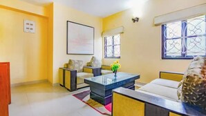 A living room with a sofa set, a coffee table, a painting on the wall, and a window with decorative iron bars.