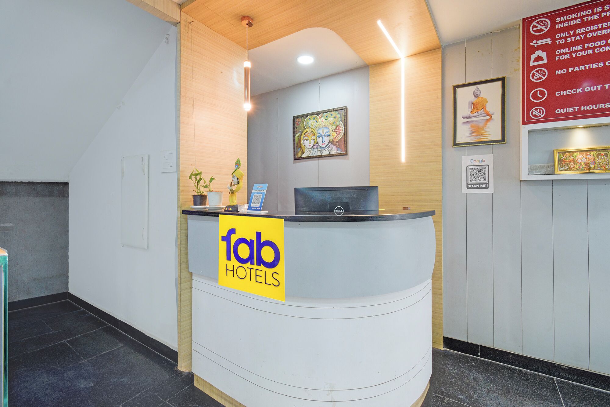 Mostrador de recepción de hotel con un letrero que dice 'fab hotels', una computadora, una planta y un cuadro en la pared.