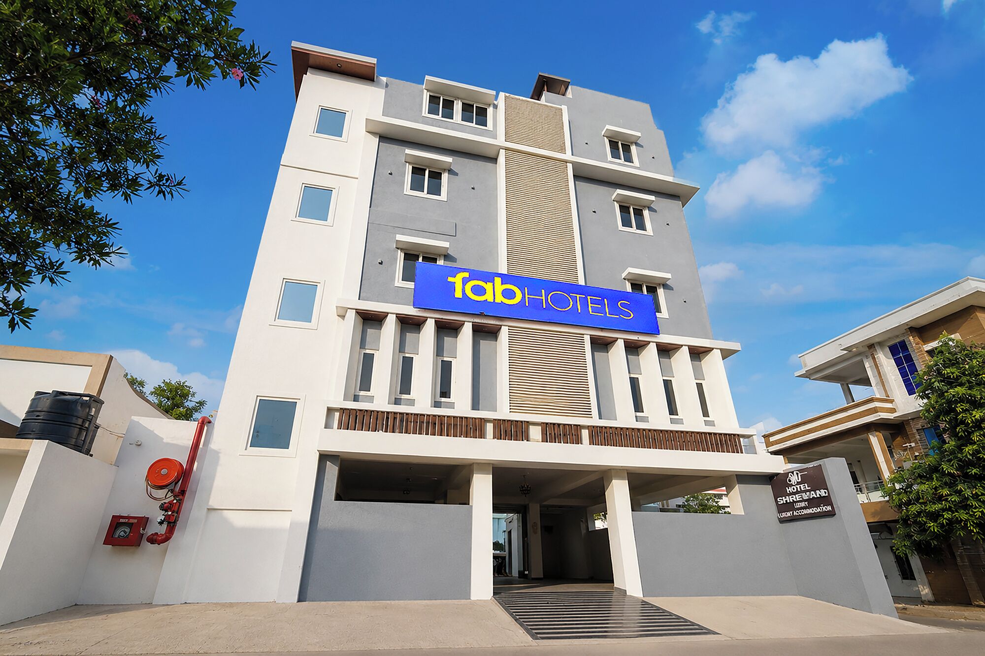 A modern hotel building with a prominent 'fab hotels' sign, a covered entrance, and a visible fire hose on the left.