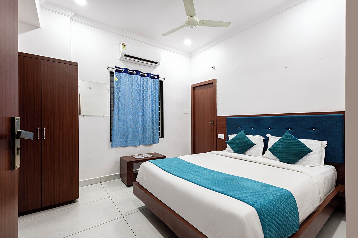 Une chambre à coucher comprenant un lit, une table de chevet, une armoire, un ventilateur de plafond et une fenêtre avec des rideaux.
