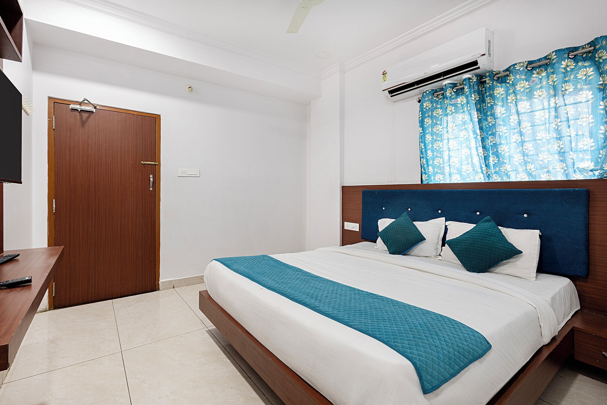 A hotel room with a bed, a desk, a TV, an air conditioner, and a window with curtains.